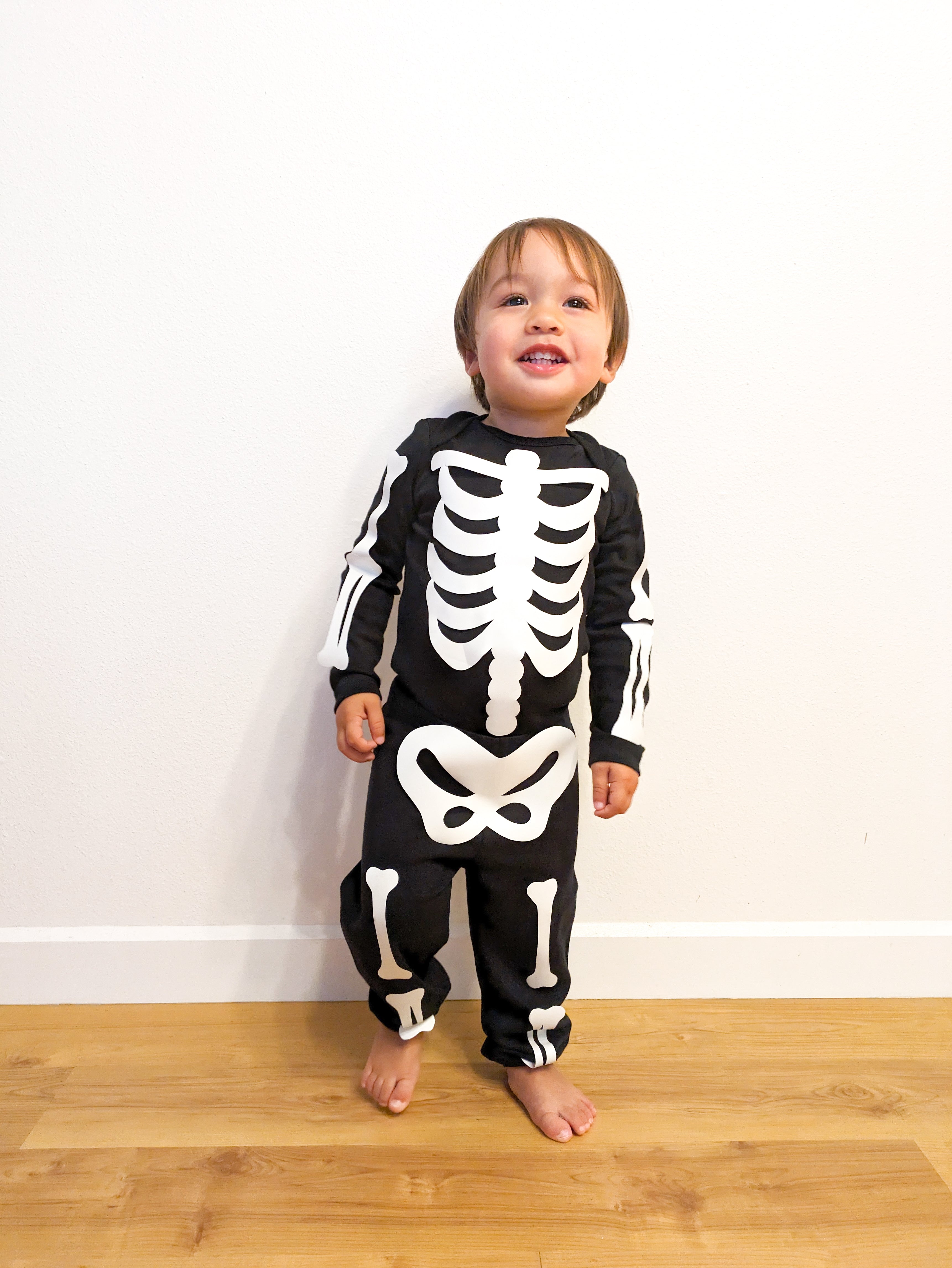 A toddler wearing a DIY skeleton costume, made from a black romper outfit