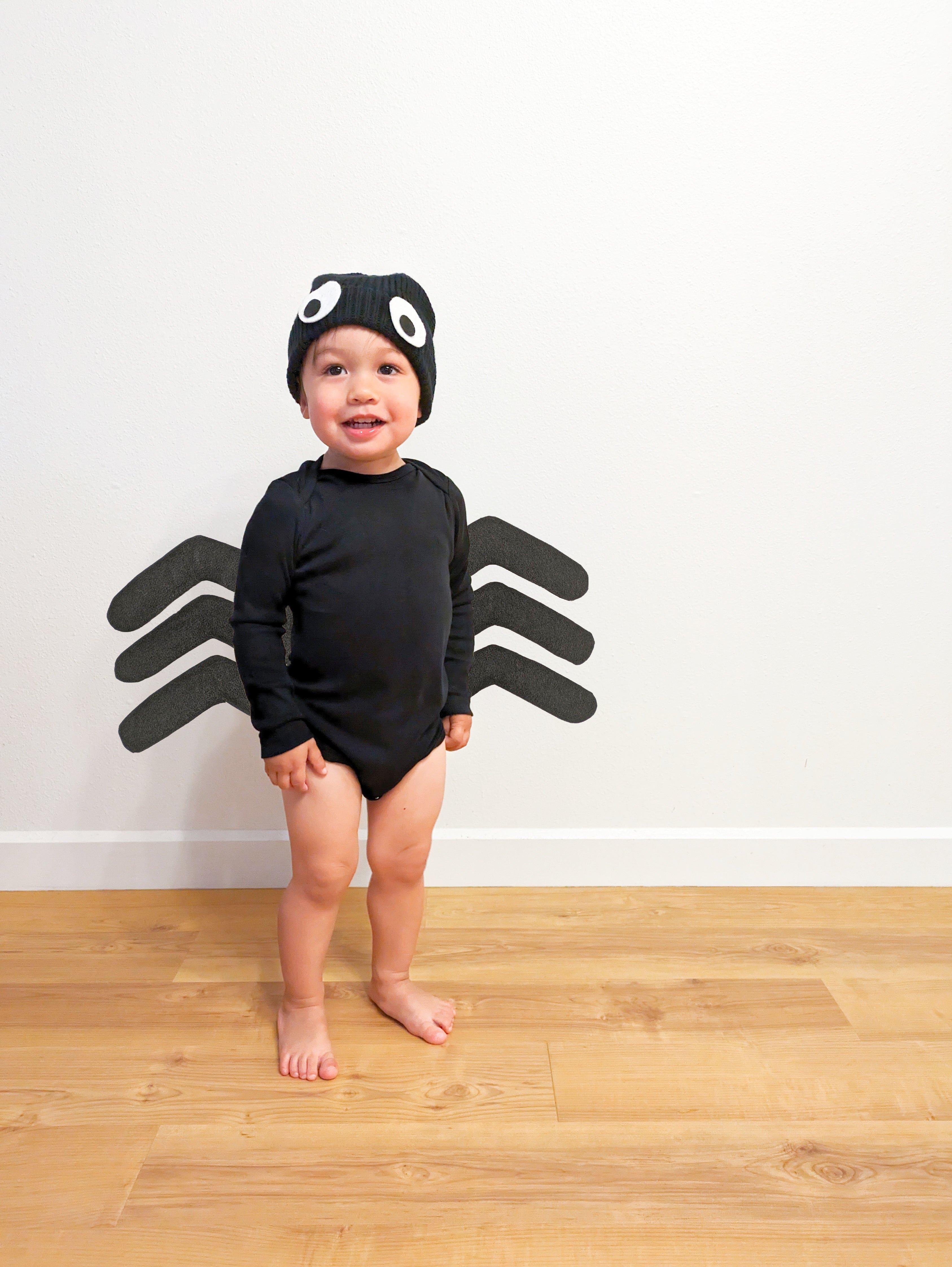 A toddler wearing a DIY Spider costumer, made with a black baby bodysuit, a black hat and homemade spider legs
