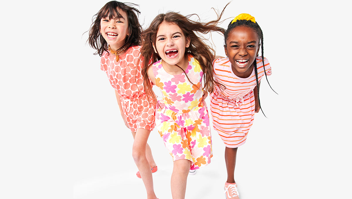 3 young children smiling and wearing colorful spring dresses with floral and stripe patterns