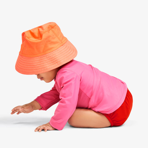 a baby crawling in a sun hat, long sleeve rash guard, and swim diaper