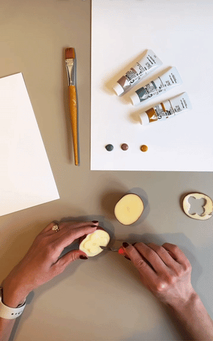 GIF of someone using a small knife to cut pieces off half a potato to create flower-shaped stamp