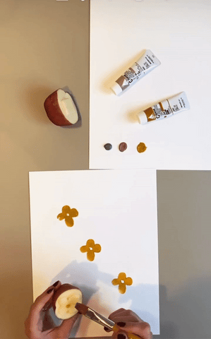 GIF of someone painting colored paint onto a flower-shaped stamp made out of a potato