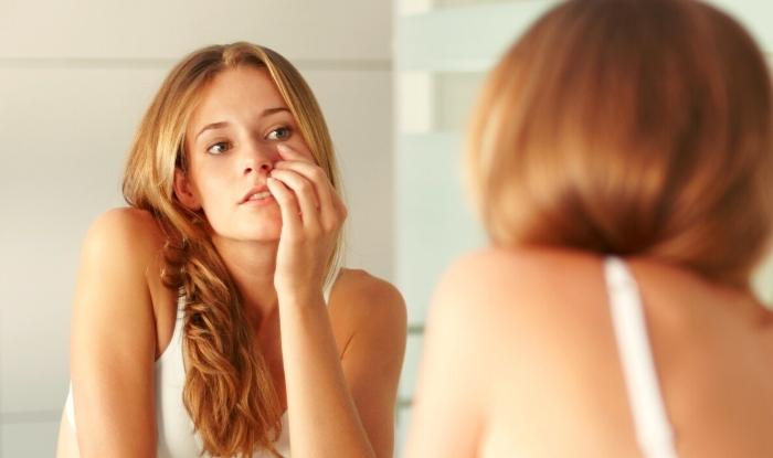 Mujer joven mirándose las ojeras y bolsas de los ojos frente al espejo.