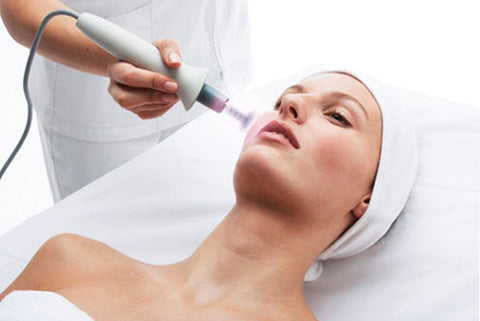 Mujer acostada recibiendo tratamiento facial en el rostro con aparato de electroporación.