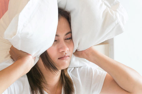 Noise can have a wide ranging impact on your sleep and life, woman covering her ears with pillow due to noise