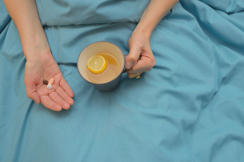 Certain medications make you feel hot while sleeping, hands on bed sheet showing medication and a tea