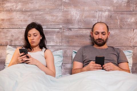 No phones or electronic devices 30 minutes before you go to sleep, couple in bed looking at phones