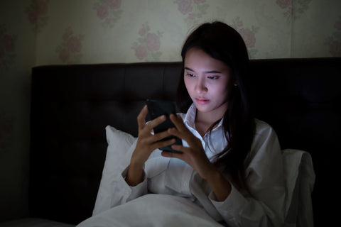 Blue light from electronic screens prehibits deep sleep, woman in bed looking at glowing phone screen
