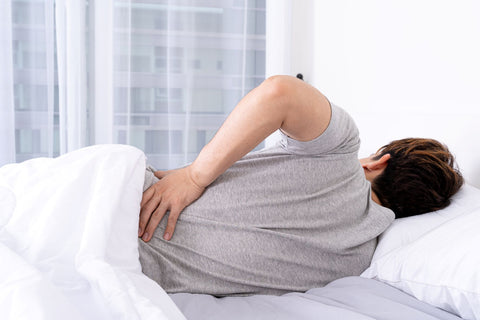 uncomfortable mattress disrupting sleep, man waking up holding his back in pain from uncomfortable bed