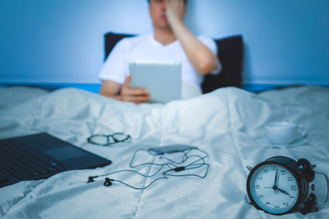 Turn Off Devices Before Bed; man in bed with all electronic devices spread out