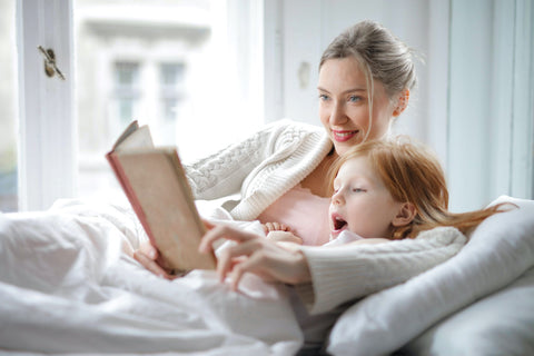 Woman reading to tired daugher child in bed