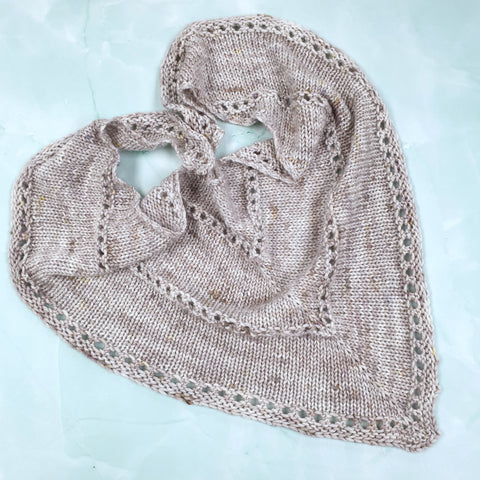 Small grey triangular shawl arranged in a heart shape on a pale blue background