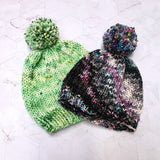 Photo of two bobble hats, one is bright green and one is black with a white section where bright coloured speckles can be seen