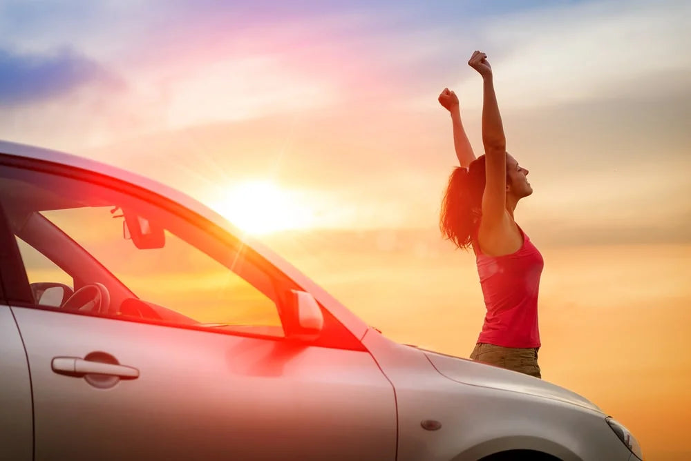 Female car driver beside her car raising arms