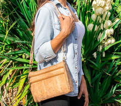 Woman wearing a natural colored cork sling bag over her shoulder in front of some flowers