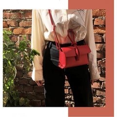 Woman wearing a red sling bag across her chest in front of a brick wall