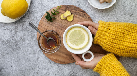 Une personne qui tient dans ses deux mains un tisane gingembre, miel, citron