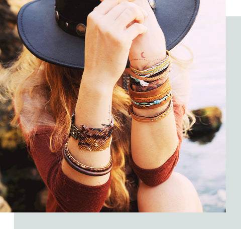 Woman with a boho hat and bracelets sitting by the water.