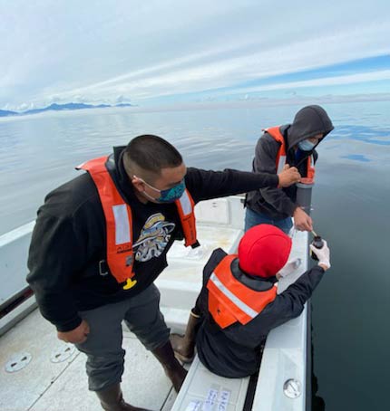 Three people on a boat collecting ocean water