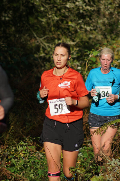 A woman trail running in black shorts and a red t shirt