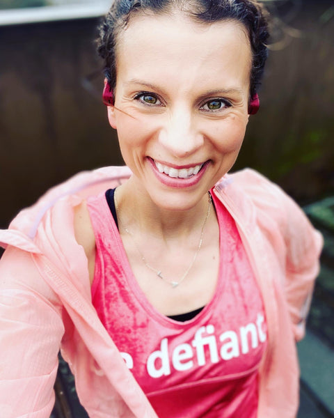 Woman with dark hair smiling while wearing a pink vest and hoodie outside