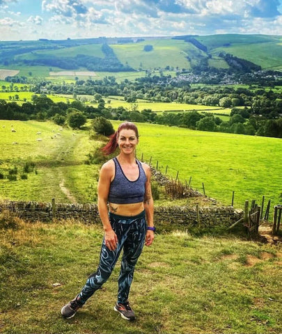 A Woman Wearing Leggings & A Sports Bra In Front Of Countryside Views