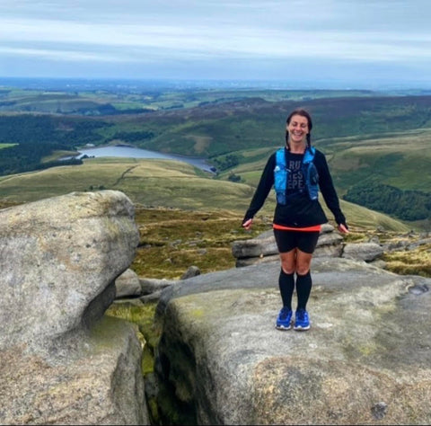 A Woman Standing On Top of A Rock In Front Of Hills Wearing Running Shoes And Long Socks