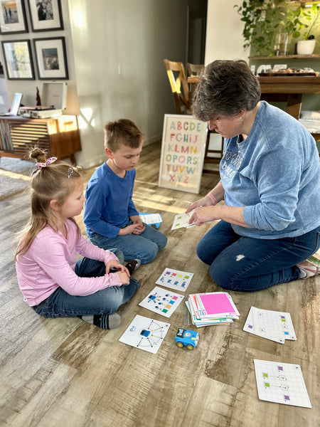 A homeschool mom and her two kids work on programming Sphero indi on their living room floor.