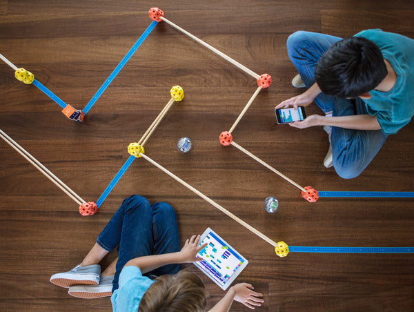 Two boys code Sphero BOLTs through a maze on the living room floor.