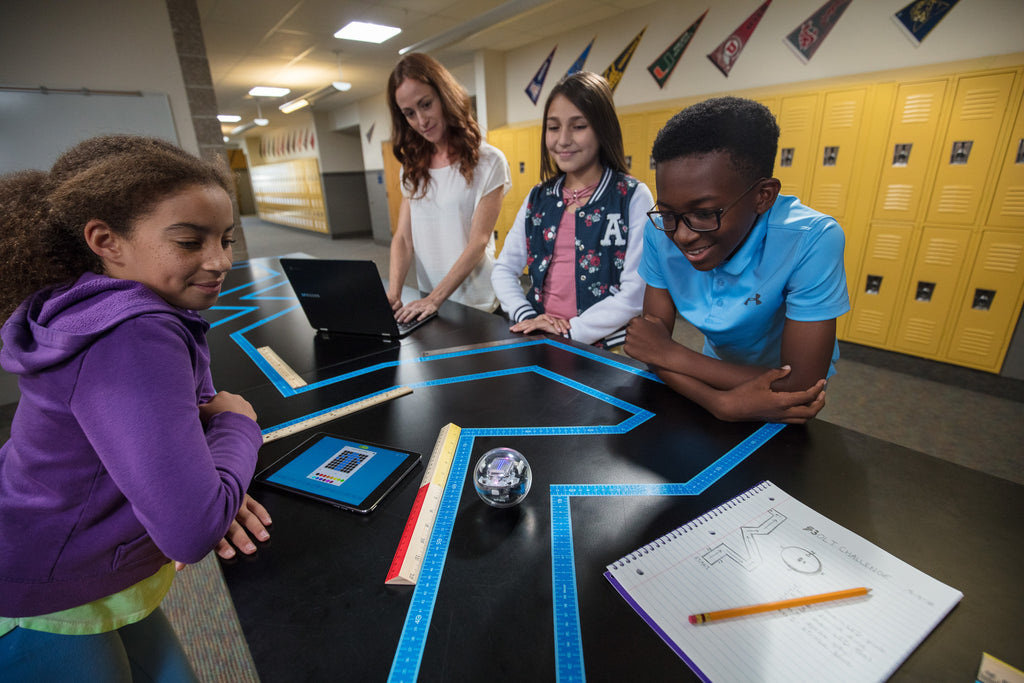 Four students watching a Sphero BOLT navigate a maze made from tape.