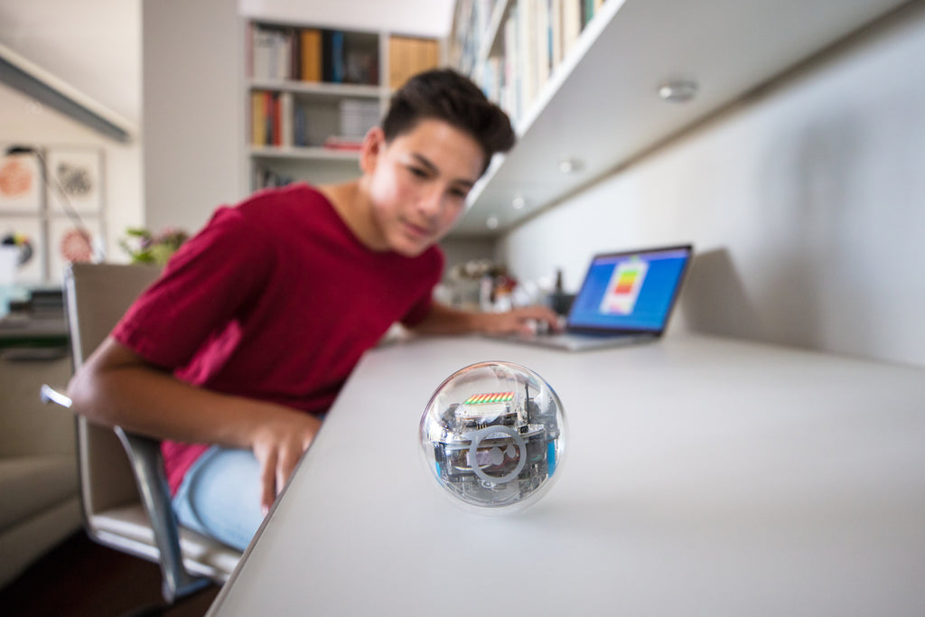 A teenage boy codes his Sphero BOLT at his desk with a laptop.