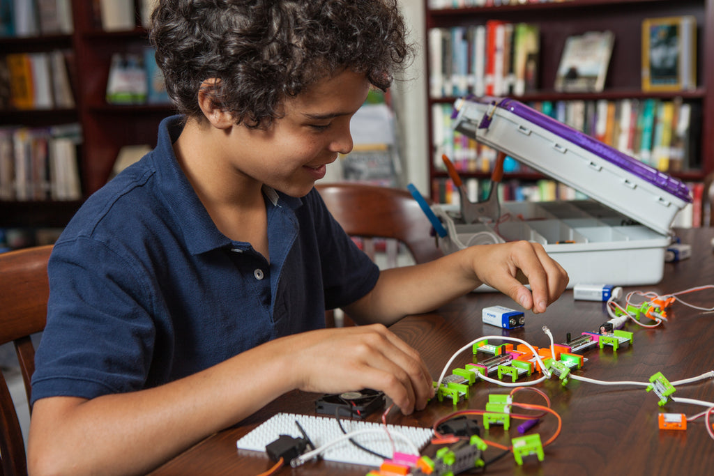 A boy builds a littleBits invention at a desk.