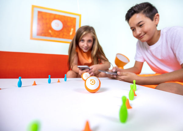 Kids coding orange Sphero mini through cones with their phones. 