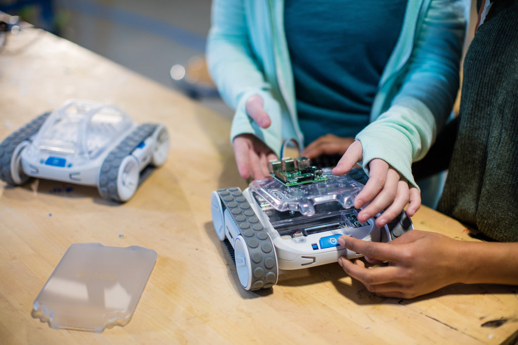 Two girls hands are shown building an invention on top of Sphero RVR. 