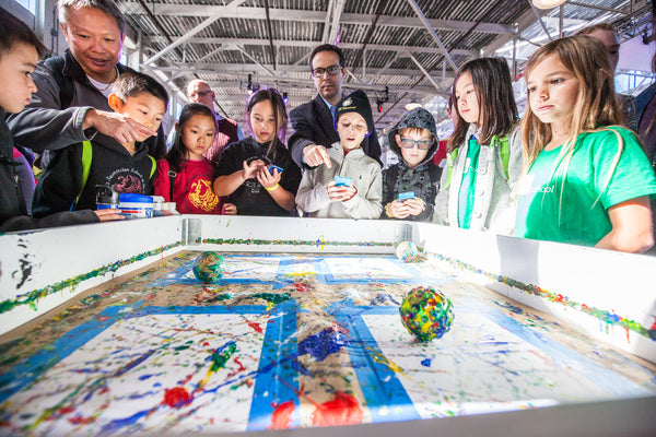 Kids stand around a table while a Sphero robot paints on paper.