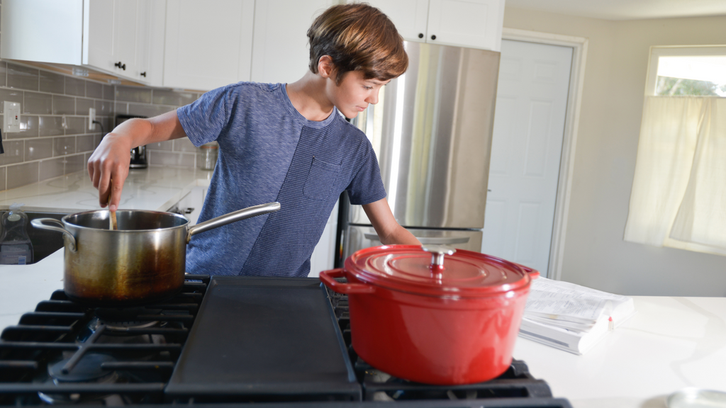 A teenage boy references a cookbook in the kitchen. Following a recipe is a good example of real-world algorithms in action.