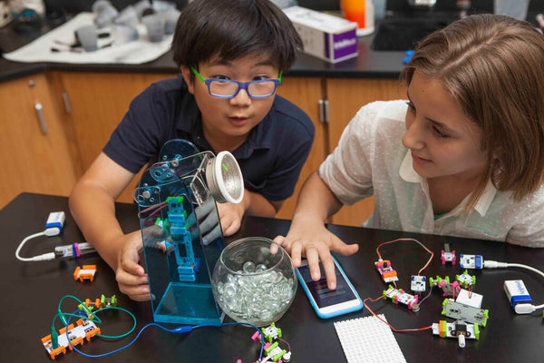 Two students create an invention with littleBits at a table in their classroom.