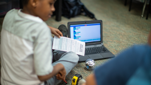 Young boy sitting on the floor with BOLT and laptop, coding robot.