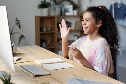 A girl sitting in front of a laptop computer at a desk raises her hand to answer a question.