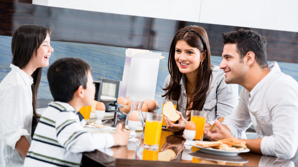 A family of four talks together over breakfast at the table.