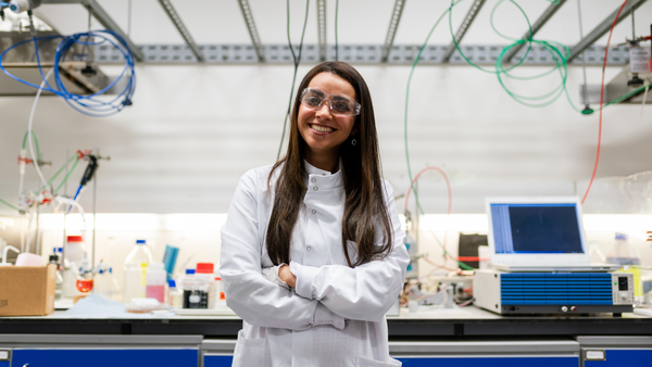 A female scientist wearing a white lab coat stands in front of the equipment in her lab.