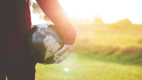 A woman's hand carrying a globe of planet earth.