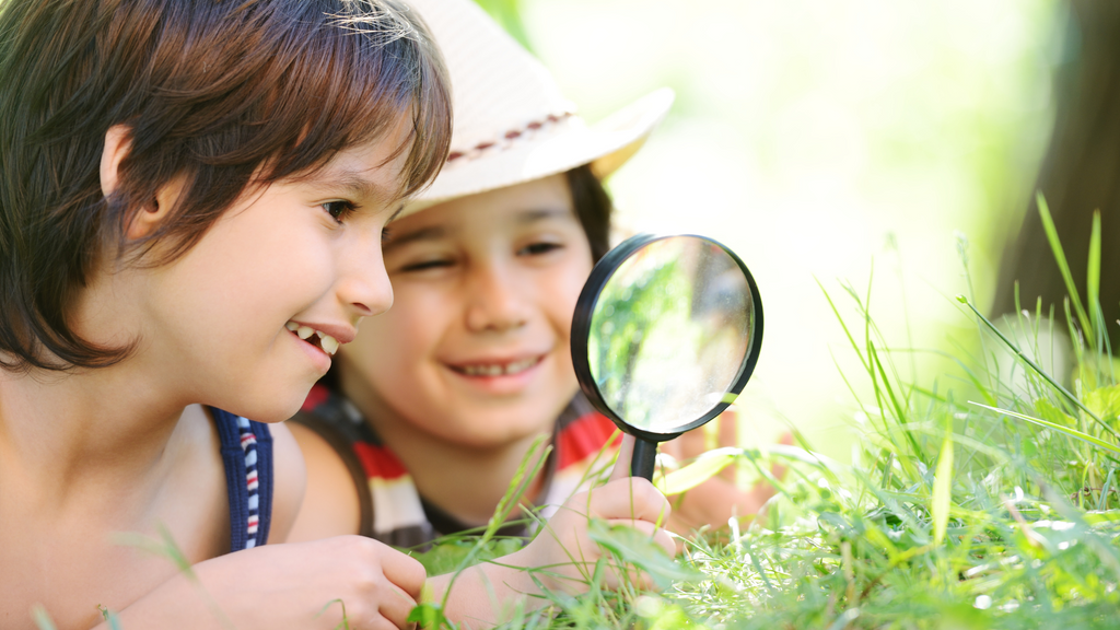 Two kids explore outside with a magnifying glass.