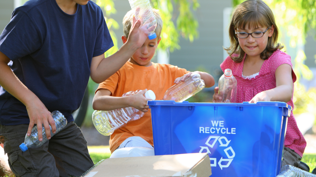 Kids put plastic bottles into a recycling bin.