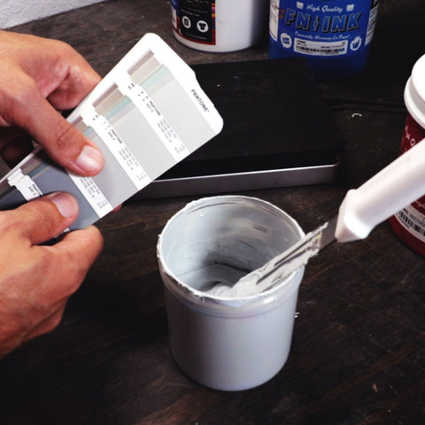 hands holding a pantone book showing gray samples next to a container with gray ink in it