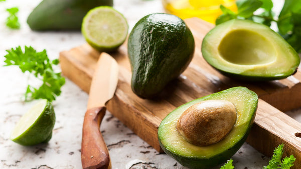 Avocados on a wooden board with a wooden knife