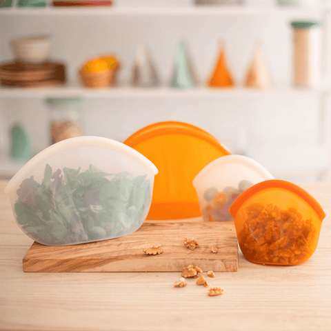 Four BPA free silicone bags on a table, three contain fruit and one is empty.