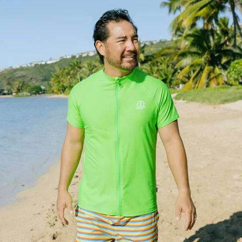 Man in a SwimZip short-sleeved rash guard walks at the beach—What is high-visibility swimwear?