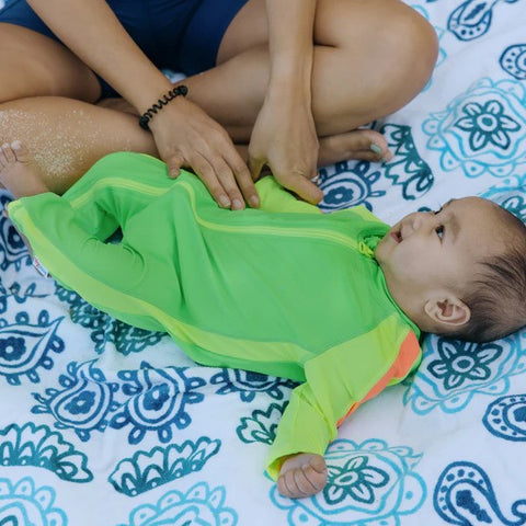 Baby in SwimZip neon green sunsuit lies on the towel—What is high-visibility swimwear?