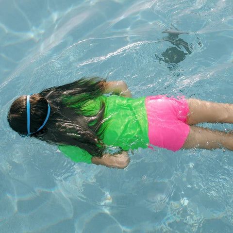 Girl in a SwimZip neon pink euro shorts swims in a pool—What is high-visibility swimwear?